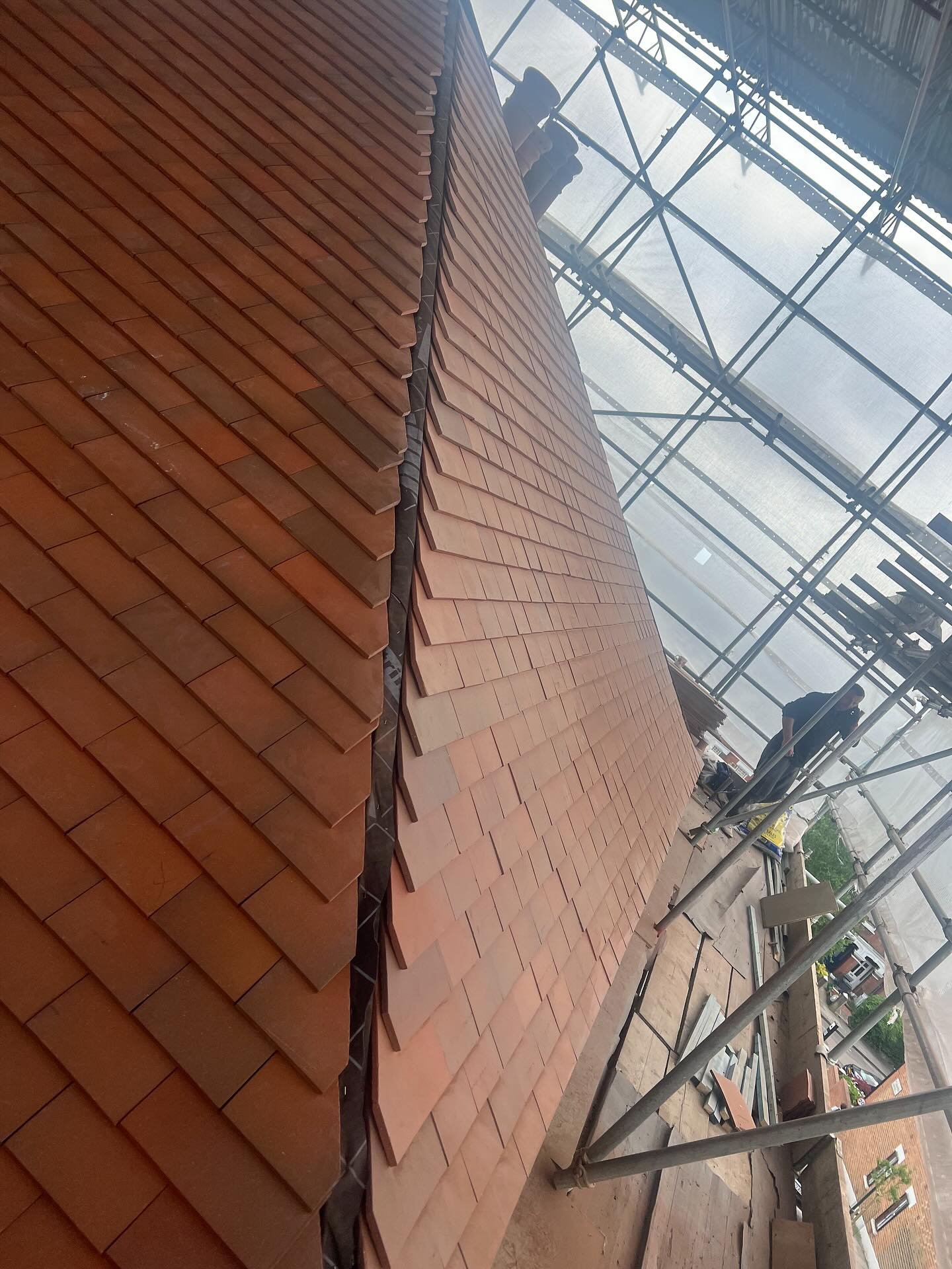 Clay tile roofing installation on a pitched roof under full scaffold cover.